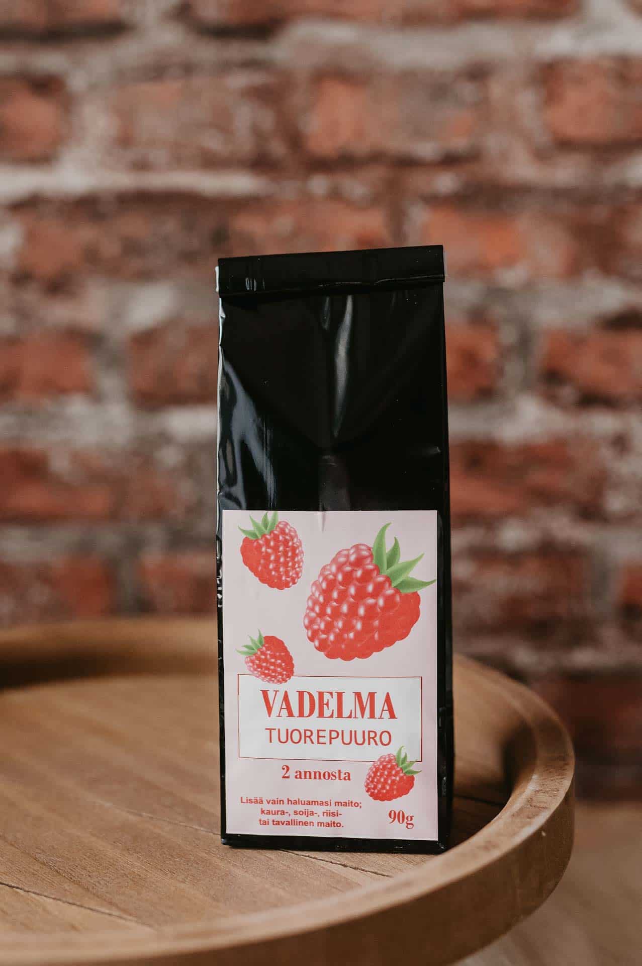 Vadelma-tuorepuuropakkaus puualustalla, taustalla tiiliseinä.