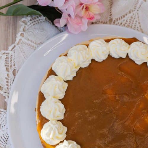Ylhäältä kuvattu Salted Caramel juustokakku – kinuskipinta ja kauniit valkoiset kermapursotukset kehystävät kakkua.