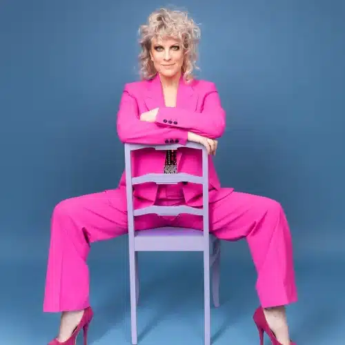 Laura Voutilainen upean pinkissä esiintymispuvussaan istuu tuolilla ja poseeraa