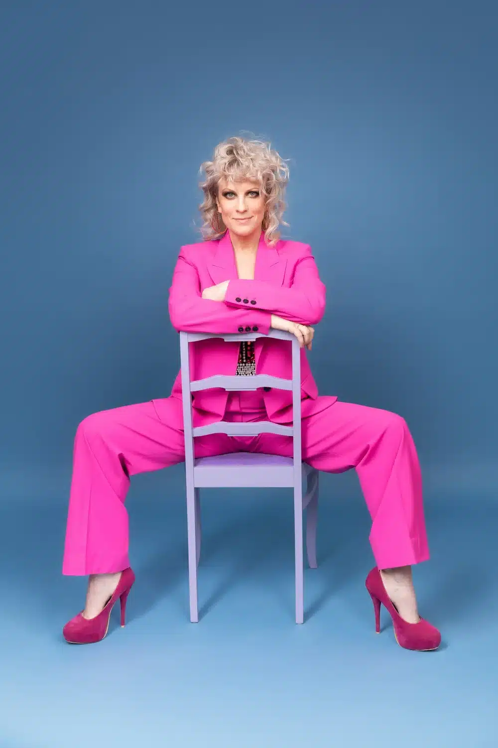Laura Voutilainen upean pinkissä esiintymispuvussaan istuu tuolilla ja poseeraa