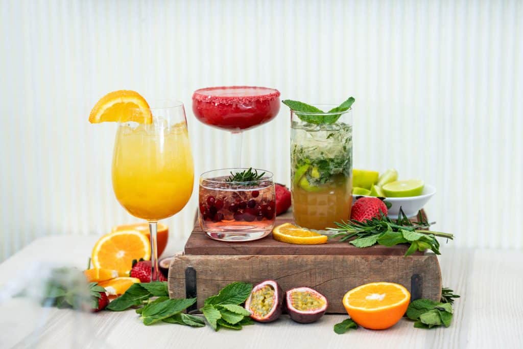 Villa Vinon Kesäkaffilan mocktailvalikoima on värikäs ja tarjoillaan kauniista laseista. Kuvassa somisteena mintun lehtiä ja sitrushedelmiä